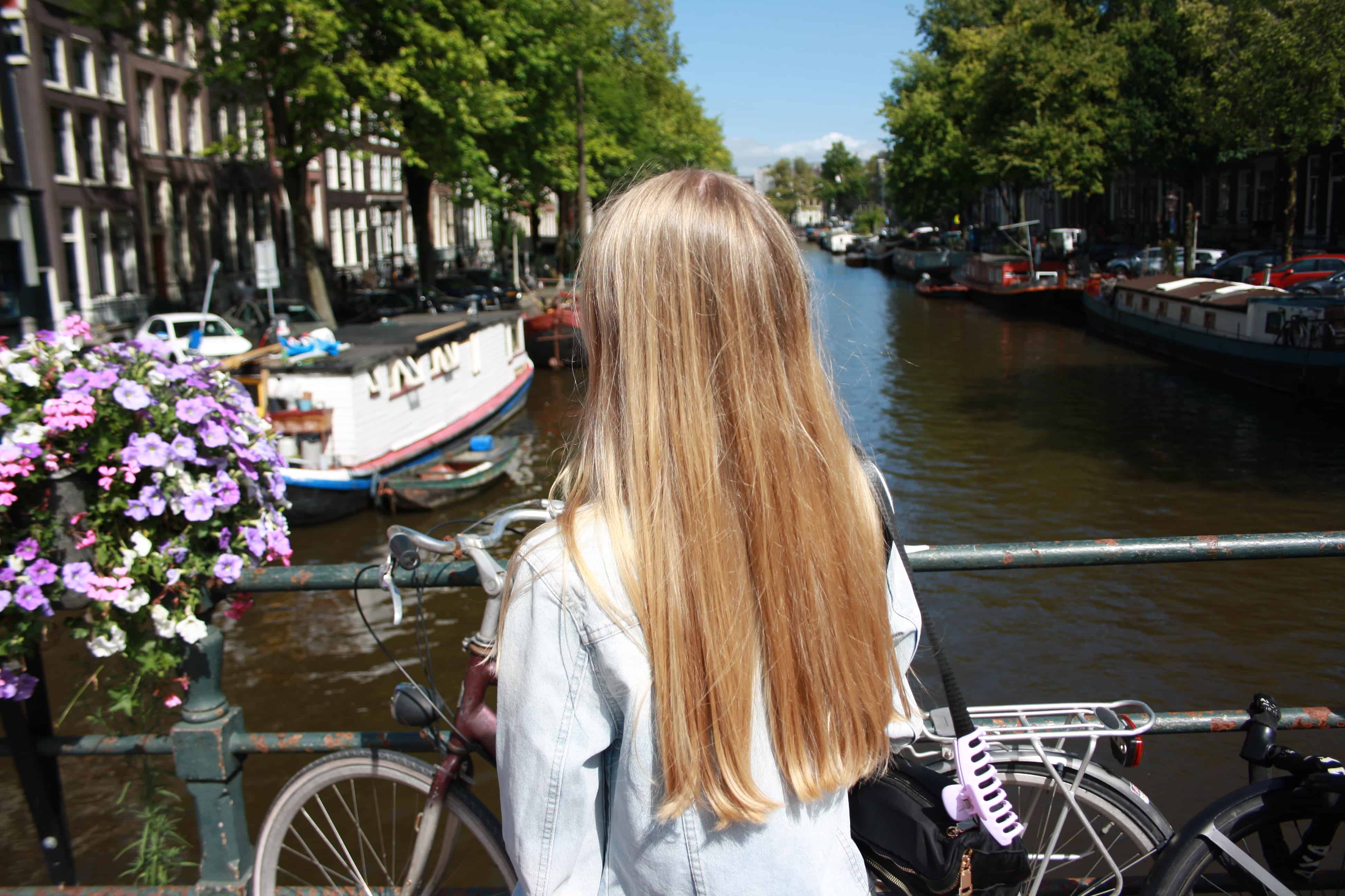 Amsterdam's canals are beautiful and one of the highlights of the city. Girl stands on bridge overlooking the canal.